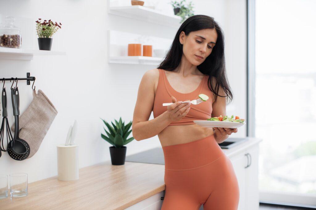 Fitness lady looking at plate with greens in modern kitchen
